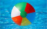 Dead centred shot from a low angle of a floating beachball in a bright blue pool