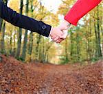 Young couple holding hands in during a walk in the autumn forest. Closeup.