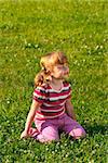 Little girl sitting on the grass in the park, dreaming of something