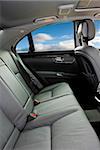 Backseat grey leather interior of a luxury car with blue skies through the windows