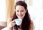 Smiling woman drinking a cup of coffee in bedroom in the morning