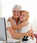 Granddaughter and grandmother hugging and using a computer at home