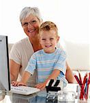 Happy grandson using a computer with his grandmother at home