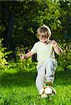 Little boy plays with a football in a summer garden