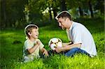 Father and son talk, sitting in park with a football