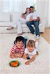 Happy children watching television on floor in living-room with their parents on sofa