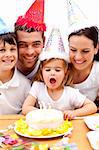 Little girl blowing out candles in her birthday's day with family