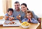 Happy parents and children eating pizza and fries at home