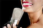 Beautiful woman singing on a vintage microphone on black background