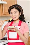 Beautiful Asian woman eating eggs with chop sticks in the kitchen