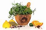 Herb leaf selection of parsley, rosemary and thyme in an olive wood mortar with pestle, lemons, oranges, and spices over white background.