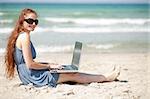 Portrait of a Woman working on a laptop by sitting on the beach