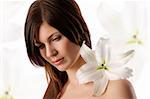 beauty portrait of pretty young woman with a big white lily on her shoulder looking sad