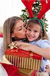 Loving mother kisses daughter at Christmas in the living-room