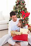 Smiling father and his daughter opening Christmas gifts at home