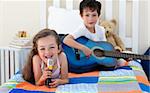 Little boy playing guitar and his sister singing in the bedroom