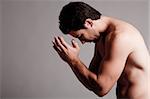 Shirtless man praying in the grey isolated background