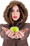 Beautiful young lady showing green apple wearing a fur coat with head cap on a white background