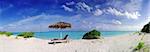 Wide panoramic photo of a beautiful Maldivian beach with parasol and two deck chairs in the front