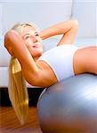 Young woman does crunches on a balance ball in the living room.  Vertical shot.