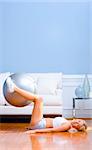 Side view of a young woman in sportswear using an exercise ball in the living room.  Vertical shot.