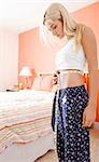 Woman standing in her bedroom and measuring her waist. Vertical format.