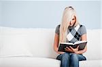 Cropped view of woman sitting on a white couch with a book. Horizontal format.