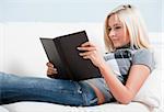 Cropped view of smiling woman relaxing on white couch with a book. Horizontal format.