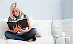 Woman sitting cross-legged on white couch and reading a book. Horizontal format.