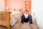 View of man facing the camera and doing sit-ups next to his bed. Horizontal format.