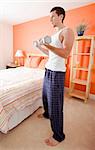 Full length view of man standing next to bed and lifting arm weights. Vertical format.