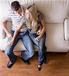 Full length overhead view of affectionate couple sitting together on white love seat. Square format.