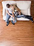 Full length overhead view of affectionate couple sitting together on white love seat. Vertical format.