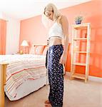Woman standing next to her bed and using a tape measure to measure her waist. Square format.