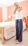 Happy woman weighing herself in her bedroom and looking down at the scale. Vertical format.