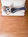 Full length overhead view of woman reclining and reading on white couch. Vertical format.