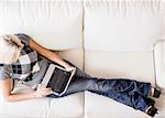 Overhead view of woman reclining on white couch and using a laptop. Horizontal format.