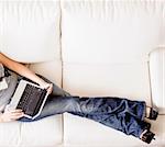 Cropped overhead view of woman reclining on white couch and using a laptop. Horizontal format.