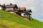 Alpine chalets on a hill. Green meadow in front. Summer time