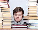 Young serious student with funny face sitting between books