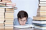 Young tired student with glass sitting between books