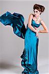 Attractive young woman standing with her hands on her hips in a blue satin, wind blown dress. Vertical shot.