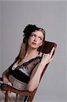 Attractive young woman wearing a black feather hairdressing and sitting in a rocking chair. Vertical shot.