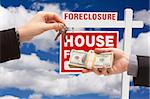 Handing Over Cash For House Keys in Front of Foreclosure Sign and Cloudy Blue Sky.