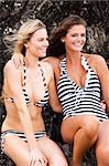 Two attractive you women wearing striped swimsuits are sitting on rocks. Vertical shot.