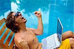 Man is happy and sits poolside with his laptop
