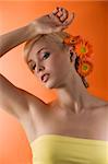 young pretty blond woman with flower in hair posing on orange background