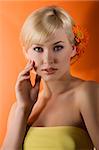 young beauty blond girl with yellow top and hair style with gerbera on orange background looking in camera