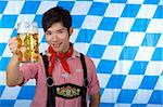 Asian Boy is holding a full Oktoberfest beer stein and smiles happy in camera. In background Bavarian flag visible.