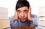 Young handsome student sitting on a desk between study books and looks frustrated. Isolated on white.